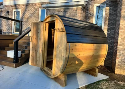 Outdoor cedar barrel sauna built by Sauna Craft with the door open and a dark metal roof
