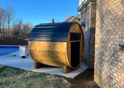 Side view of an outdoor cedar sauna built by Sauna Craft, on a concrete pad near the pool