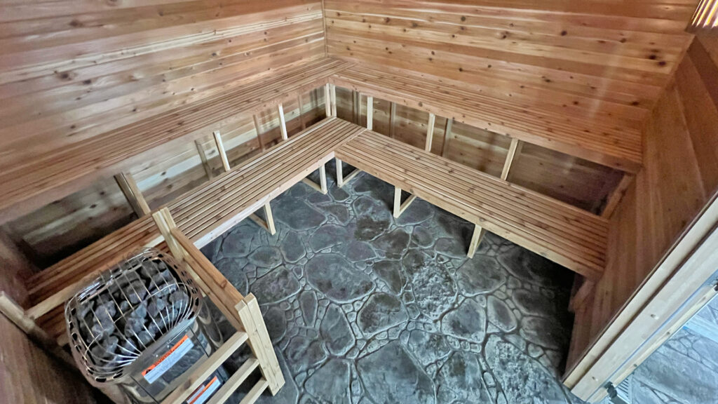 L-shaped cedar benches and a rock heater behind a wood guard inside the YMCA Kokomo sauna built by Sauna Craft