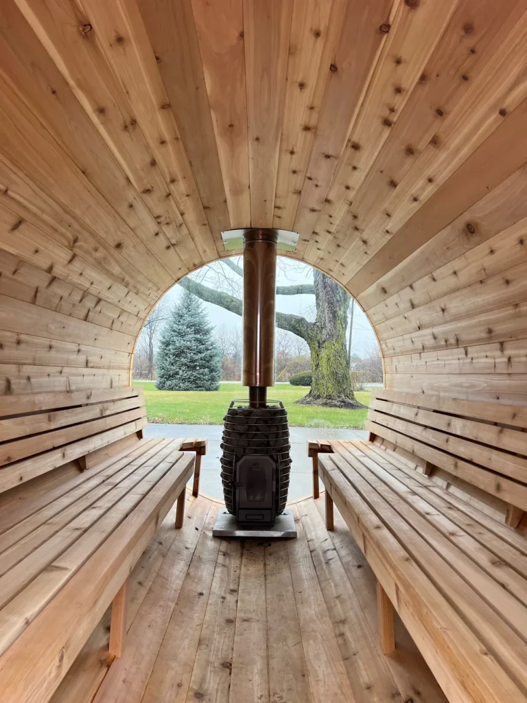 Inside the finished custom trailer sauna: a wood-burning stove with a stone cage between two cedar benches, glass back wall